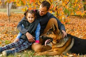 joven familia con un perro en hojas en un otoños día foto