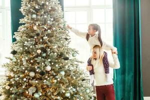 Happy family woman mother and little girl relax playing sparkler near Christmas tree on Christmas eve at home. Mom, daughter in house with winter decoration. Christmas New Year time for celebration photo