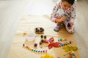 little child making autumn decoration from chestnut, pine cones and acorns photo