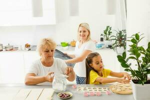 Little girl learning to roll dough and make homemade pastry or cookies with her mother and grandmother photo