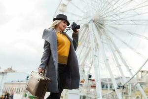 Attractive blonde girl in casual clothing, wearing a coat, holding a brown retro suitcase in his hands, background of the ferris wheel photo