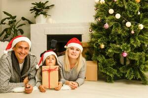 Family gather around a Christmas tree, holding a present photo