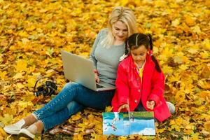 mother and daughter work on laptop outside in autumn. photo