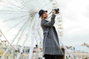 Stylish lady walking around city. Outdoor photo of pretty girl with charming smile posing in gray coat on urban background ferris wheel