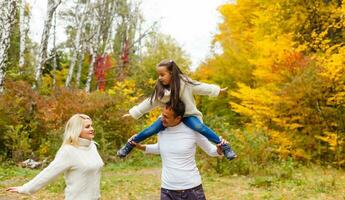 imagen de encantador familia en otoño parque, joven padres con bonito adorable hija jugando al aire libre, tener divertido en patio interior en caer, contento familia disfrutar otoñal naturaleza foto