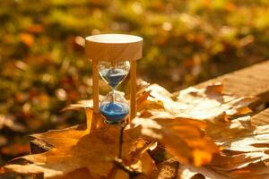 otoño hora tema, reloj de arena en caído hojas en varios colores con Copiar espacio. foto