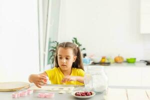 little girl makes cookies from the dough in the kitchen at home photo