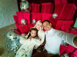 familia, vacaciones, tecnología y personas - sonriente madre, padre y pequeño niña haciendo selfie con cámara terminado vivo habitación y Navidad árbol antecedentes foto