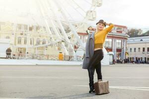 Young woman wearing hat walking outdoors on the city street near ferris wheel smiling cheerful. photo