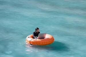 Businessman using laptop computer on an inflatable donut in the sea. Summer vacation concept. Generative AI photo