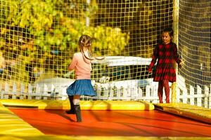 dos pequeño muchachas saltando en un trampolín a un otoño justa foto