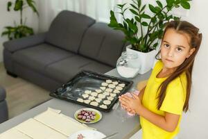 pequeño niña hace galletas desde el masa en el cocina a hogar foto