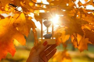 otoño hora tema, reloj de arena en caído hojas en varios colores con Copiar espacio. foto