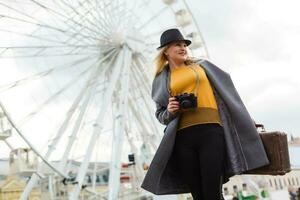 Young woman wearing hat walking outdoors on the city street near ferris wheel smiling cheerful. photo