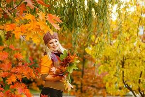 Young woman with autumn leaves in hand and fall yellow maple garden background photo