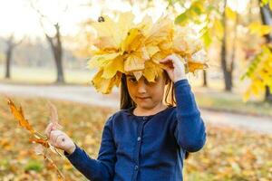 contento pequeño niño, niña riendo y jugando en el otoño en el naturaleza caminar al aire libre foto