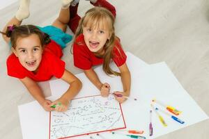 familia, ocio y infancia concepto - contento hermanas acostado en piso y dibujo y haciendo deberes a hogar foto