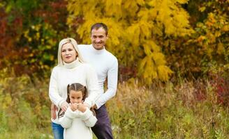 Picture of lovely family in autumn park, young parents with nice adorable daughter playing outdoors, have fun on backyard in fall, happy family enjoy autumnal nature photo