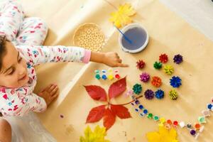 linda pequeño niña colorante un natural cono abeto a crear un flor, conjunto de cepillos, pinturas, natural otoño materiales, crear divertido y fácil con niños, bricolaje para jardín de infancia foto