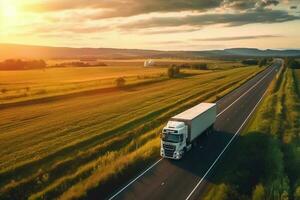 Big blue truck driving fast with a white trailer with blank space for text on a countryside road with other cars against a blue sky with a sunset Generative AI photo