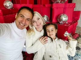 familia, vacaciones, tecnología y personas - sonriente madre, padre y pequeño niña haciendo selfie con cámara terminado vivo habitación y Navidad árbol antecedentes foto