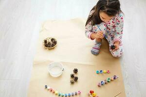 linda pequeño niña colorante un natural cono abeto a crear un flor, conjunto de cepillos, pinturas, natural otoño materiales, crear divertido y fácil con niños, bricolaje para jardín de infancia foto