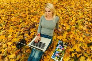 mujer con ordenador portátil y foto libro en otoño parque