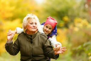 Happy senior lady and a little toddler girl, grandmother and granddaughter, enjoying a walk in the park. Child and grandparent. autumns day. Grandmother and little girl happy together in the garden photo