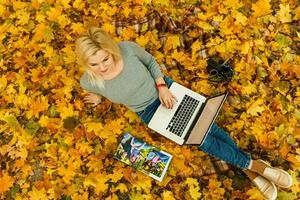 woman with laptop and photo book in autumn park