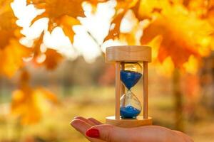 otoño hora tema, reloj de arena en caído hojas en varios colores con Copiar espacio. foto