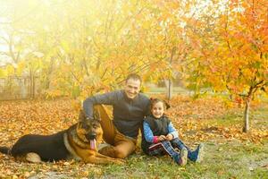 joven familia con un perro en hojas en un otoños día foto