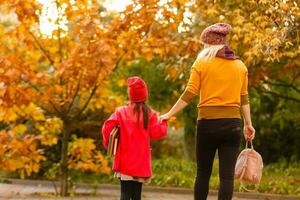 padre tomar niño a escuela. alumno de primario colegio con mochila al aire libre. madre y hija Vamos mano en mano. espalda a escuela. primero día de caer. elemental alumno. jardín de infancia, preescolar. foto