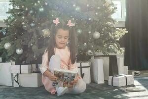little girl looking photobook in front of Christmas tree photo