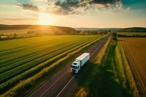 Big blue truck driving fast with a white trailer with blank space for text on a countryside road with other cars against a blue sky with a sunset Generative AI photo