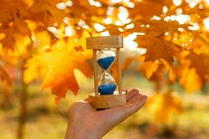 otoño hora tema, reloj de arena en caído hojas en varios colores con Copiar espacio. foto