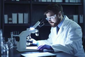 Bearded laboratory scientist or doctor using laptop computer and microscope for researching information at laboratory. Smiling caucasian university student studying medicine. photo