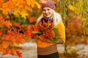 Young woman with autumn leaves in hand and fall yellow maple garden background photo