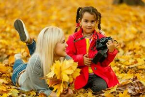pequeño niña obras de teatro con un cámara en amarillo hojas de otoño paisaje foto