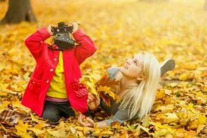 little girl plays with a camera in yellow leaves of autumn landscape photo