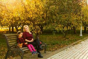 contento madre y hija abrazando en un banco en un otoño parque foto