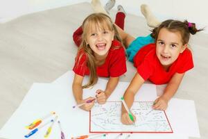 family, leisure and childhood concept - happy sisters lying on floor and drawing and doing homework at home photo