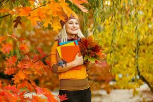 joven mujer con otoño hojas en mano y otoño amarillo arce jardín antecedentes foto