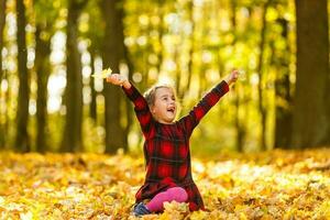 Little girl collects fallen autumn leaves. photo