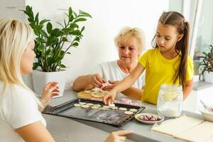 Little girl learning to roll dough and make homemade cookies with her mother and grandmother photo