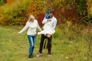 imagen de encantador familia en otoño parque, joven padres con bonito adorable hija jugando al aire libre, tener divertido en patio interior en caer, contento familia disfrutar otoñal naturaleza foto