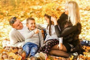 sonriente joven familia sentado en hojas en un otoños día foto