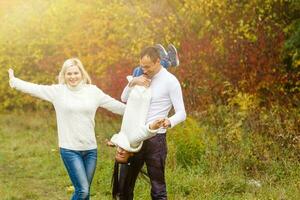 imagen de encantador familia en otoño parque, joven padres con bonito adorable hija jugando al aire libre, tener divertido en patio interior en caer, contento familia disfrutar otoñal naturaleza foto