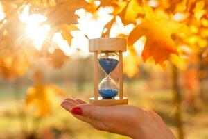 otoño hora tema, reloj de arena en caído hojas en varios colores con Copiar espacio. foto