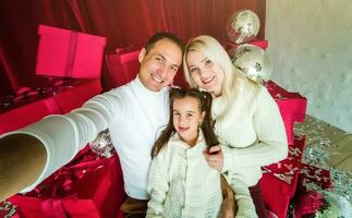 Christmas. Family. Technology. View on the smartphone. Dad, mom and daughter looking at camera and smiling while doing selfie photo