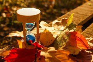 otoño hora tema, reloj de arena en caído hojas en varios colores con Copiar espacio. foto